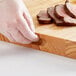 A person's gloved hand using a Choice wooden cutting board to cut meat.