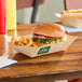 A rectangular compostable bamboo food tray containing a sandwich and curly fries on a wooden table.