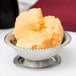 A stainless steel Vollrath sherbet dish filled with orange ice cream.