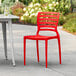 A red Lancaster Table & Seating Sol Buoy resin chair on a patio next to a table.