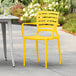 A Lancaster Table & Seating Sol yellow resin arm chair on a patio.