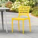 A Lancaster Table & Seating yellow resin chair on a patio.