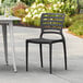 A black Lancaster Table & Seating Sol resin chair on a white table on an outdoor patio.