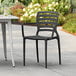 A black Lancaster Table & Seating Sol resin arm chair on a tile patio.