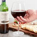 A hand holding a Stolzle Exquisit burgundy wine glass next to a bottle of wine.
