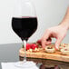 A hand reaching for a Stolzle Exquisit wine glass filled with red wine on a table