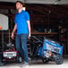 A man in a blue shirt and jeans walking with a Westinghouse WGen7500 generator in a garage.