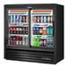 A black True refrigerated glass door merchandiser with drinks inside.