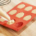 A person using a pastry bag to fill a Madeleine mold with White Toque Madeleine batter.