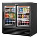 A True refrigerated sliding glass door merchandiser with LED lighting filled with drinks in a convenience store.
