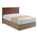 A bed with a 1888 Mills Beyond Impressions beige striped top sheet on a bed with a wood headboard.