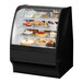 A True black refrigerated bakery display case on a counter with cakes inside.