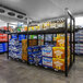 A Wanzl beer cave cooler shelving unit in a convenience store filled with beer bottles and boxes.