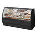 A True black refrigerated bakery display case with curved glass containing different cakes.
