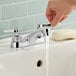 A hand washing under an American Standard deck-mount faucet.