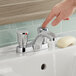 A finger pressing a button on an American Standard deck-mount metering faucet.