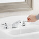 A hand pressing the American Standard Monterrey widespread faucet over a sink.