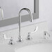 An American Standard deck-mount widespread faucet with two gooseneck spouts over a white sink.