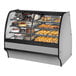 A True dual zone bakery display case with a curved glass front and stainless steel interior filled with various pastries.
