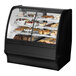 A True dual zone bakery display case with curved black glass shelves holding various pastries.