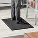 A person standing on a black Choice anti-fatigue floor mat in a kitchen.