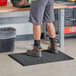 A person standing on a Choice black anti-fatigue floor mat.