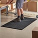 A person standing on a black Choice anti-fatigue floor mat with drainage holes.