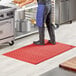 A man standing on a red Lavex anti-fatigue floor mat in a professional kitchen.