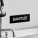 A black and white Lavex Sanitize sign with white text on a wall.