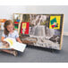 A young girl sitting on the floor reading a book from a Whitney Brothers wood book display.