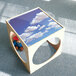 A wooden cube with a picture of a blue sky and clouds on it.