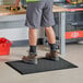 A person standing on a Lavex Heavy-Duty Black Anti-Fatigue Floor Mat.