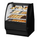 A True curved glass black dry bakery display case with various types of pastries on shelves with a white interior.