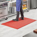 A person standing on a red Choice anti-fatigue floor mat in a kitchen.