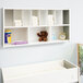 A green and white Whitney Brothers wall-mount diaper supply cabinet with shelves holding diapers and toys.