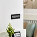 A Lavex black and white reserved sign on a wall next to a green flower in a vase.