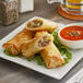 A plate of fried Gourmet Egg Roll Co. Philly Cheesesteak Egg Rolls with dipping sauce.