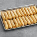 A tray of 60 Gourmet Egg Roll Co. Egg and Cheese Egg Rolls on a gray surface.