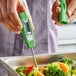 A green digital pocket probe thermometer being used to measure the temperature of cooked vegetables.