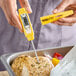 A yellow digital pocket probe thermometer being used to check the temperature of cooked chicken.