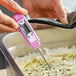 A purple digital pocket probe thermometer being used to measure the temperature of food in a metal container.