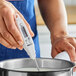 A white digital pocket probe thermometer being used to measure the temperature of liquid in a pot.