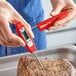 A red digital pocket probe thermometer being used to check the temperature of cooked meat.