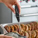 A black digital pocket probe thermometer being used to check the temperature of cooked meat in a tray.