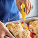 A yellow digital pocket probe thermometer being used to check the temperature of cooked chicken.