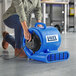 A woman using a Lavex blue air mover to dry a floor in a professional kitchen.