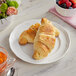 A plate of Brioche Gourmet plant-based croissants next to a bowl of fruit.