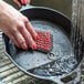 A hand using a Lodge chainmail scrub pad with red silicone to wash a pan.