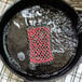 A red and black Lodge chainmail scrub pad on a black frying pan.