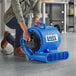 A woman using a Lavex blue compact air mover to dry the floor in a professional kitchen.